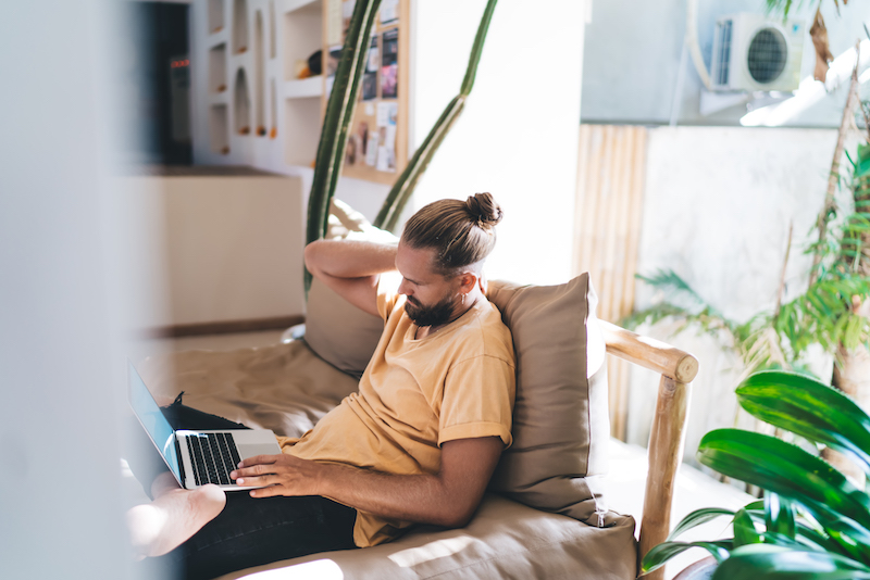 Modern Millenial Male with a top knot sits at a laptop as he begins his job search.