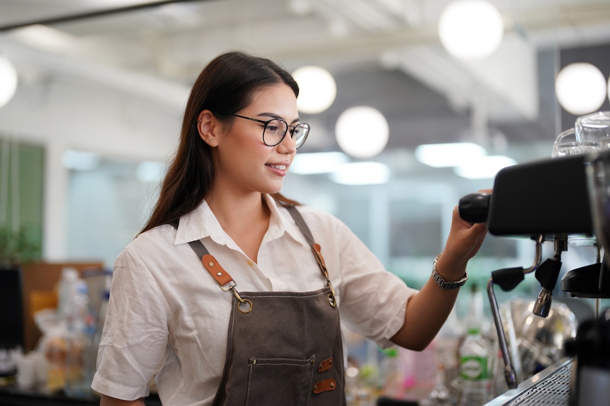 A smiling female barista is busy at the counter while working in a popular part time job hiring near Dallas.