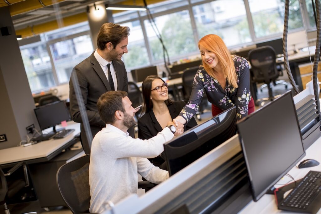 A male and female collegue shake hands in an office as a show of high emotional intelligence.